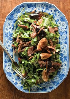 a blue and white bowl filled with salad on top of a wooden table next to a fork