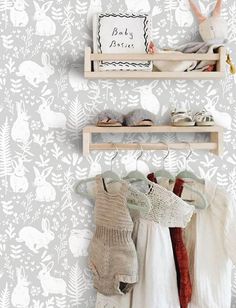 two wooden shelves filled with baby clothes next to a wallpaper covered in white leaves