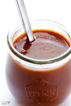 a jar filled with sauce and a spoon sticking out of the top, on a white surface