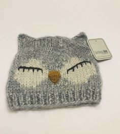 a knitted owl hat with eyes and nose on white table next to small tag