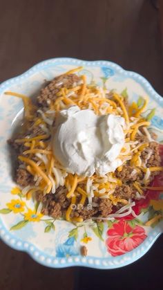 a white and blue plate topped with taco meat covered in sour cream on top of a wooden table