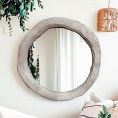 a round mirror hanging on the wall next to a bed with pillows and plants in it