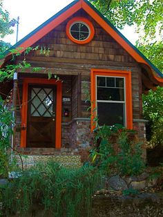 a small house with an orange trim and window on the front door is surrounded by greenery