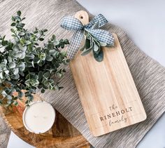 a wooden cutting board sitting on top of a table next to a candle and potted plant