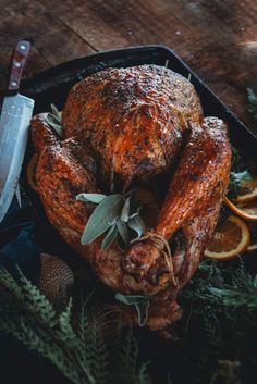 a roasted turkey on a platter with oranges and herbs next to a knife