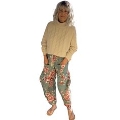 a woman standing in front of a white background wearing floral print pants and a sweater