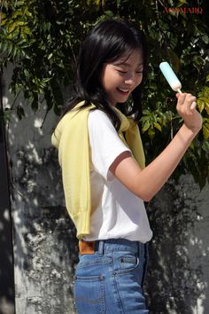 a woman holding a toothbrush in her right hand while standing next to a tree