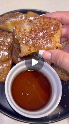 someone is dipping sauce onto some pastries on a black and white plate with powdered sugar