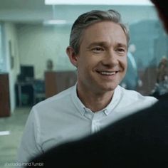 a man in a white shirt is smiling and talking to another man with grey hair