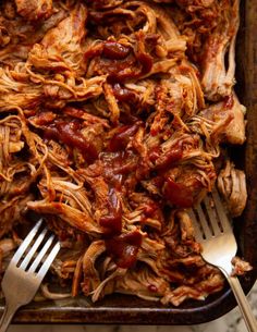 shredded meat and sauce in a baking dish with two forks on the side, ready to be eaten