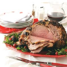 a large roast on a red platter with greens and cranberries next to silverware