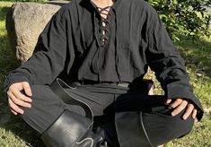 a man sitting on the ground with his hands in his pockets, wearing a black shirt and tie