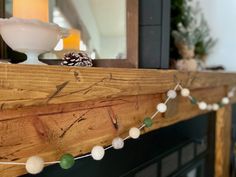 a wooden mantle decorated with pine cones and white balls on it's edge, along with other decorations