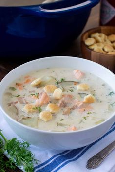 a white bowl filled with soup next to some crackers and a blue casserole dish