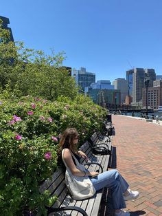 a woman sitting on a bench in front of flowers and the cityscape behind her