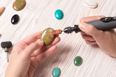 a woman is using an electric drill to paint rocks on a table with other stones