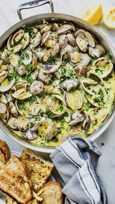 a pan filled with clams and bread on top of a table next to lemon wedges