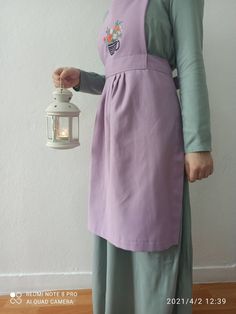 a woman in a purple apron holding a white lantern with the light on it's side