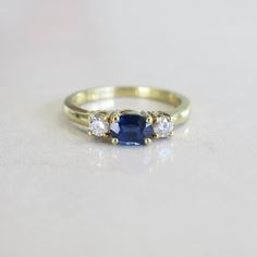 Sapphires and diamonds are the perfect pairings. This sapphire is set east to west and adorned with two bright white round brilliant diamonds set in 18k yellow gold. Metal: 18K Yellow Gold Sapphire: 6 x 4.5 MM Diamonds: .20 CTW VS1-2 G Size: 6 For a greater selection of jewelry please visit our website at www.BlackMarketLLC.com If you have any questions about this product or if we can help you with any of our other products please contact us through Etsy or our website at www.blackmarketllc.com. Sapphire And Diamond Three Stone Ring, Classic Sapphire Diamond Ring With Brilliant Cut, Formal Three Stone Sapphire Diamond Ring, Classic Cubic Zirconia Sapphire Ring, Gold Three-stone Sapphire Ring With Diamonds, Sapphire Diamond Ring With Single Cut Diamonds For Anniversary, Timeless Brilliant Cut Sapphire Diamond Ring, Gold Sapphire Ring With Three Diamonds, Timeless Sapphire Diamond Ring With Brilliant Cut