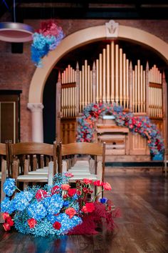 two wooden chairs with flowers on them in front of a pipe organ and an arch