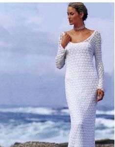 a woman standing on top of a beach next to the ocean wearing a white dress