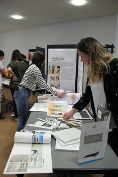 people standing around a table with some papers on it and one woman pointing at something