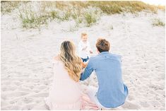 a man, woman and child sitting on the sand at the beach playing with each other