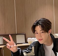 a young man sitting at a desk making the peace sign