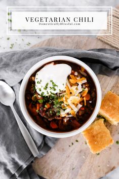 a bowl of vegetarian chili with cheese and sour cream on top, sitting on a cutting board