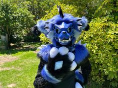 a blue and white dragon mascot standing in the grass with his hands on his chest