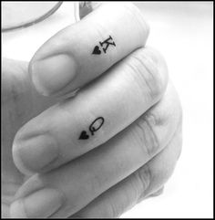 two fingers with small tattoos on them, one has an arrow and the other has a heart