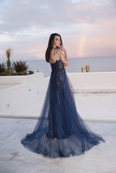 a woman in a blue dress is standing on the roof looking at the ocean with a rainbow in the background