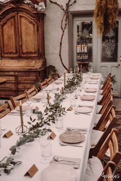 a long table is set with place settings and greenery for an outdoor dinner party