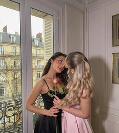 two young women standing next to each other in front of a window with a rose