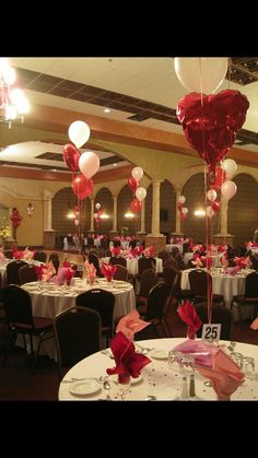 a banquet hall with tables and chairs decorated for valentine's day, filled with heart - shaped balloons