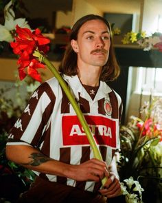 a man with long hair holding a flower in his hand and looking at the camera