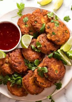 several crab cakes on a white plate with limes, cilantro and ketchup