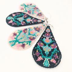 two pairs of beaded earrings with tears hanging from hooks on a white surface