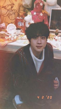 a young man sitting in front of a desk with stuffed animals on the wall behind him