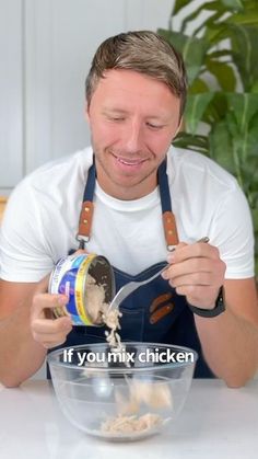 a man in an apron is pouring chicken into a bowl with a spoon and whisk