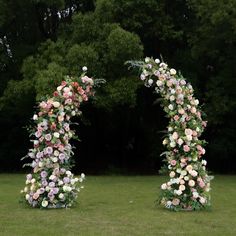 two floral archways in the middle of a grassy area with trees in the background