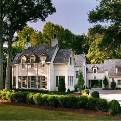 a large white house with lots of windows and bushes in front of the house is surrounded by trees