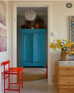 a blue cabinet sitting in the corner of a room next to a red chair and yellow flowers