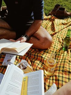 a man sitting on the grass with an open book and beer in front of him