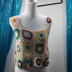 a white mannequin wearing a multicolored crochet top with flowers on it