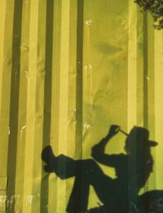 the shadow of a person holding a skateboard in front of a yellow striped wall