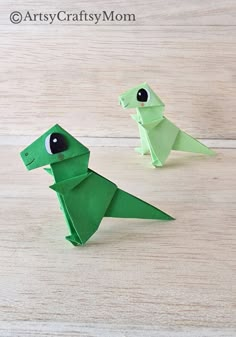 two green origami dinosaurs sitting on top of a wooden table