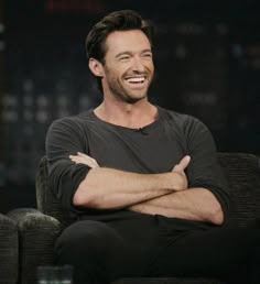 a smiling man sitting in a chair with his arms crossed