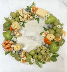 an arrangement of fruits and cheeses arranged in a circle on a marble countertop