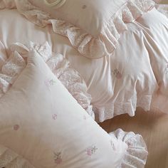 a bed with pink and white pillows on it's sides, along with lace trim around the edges